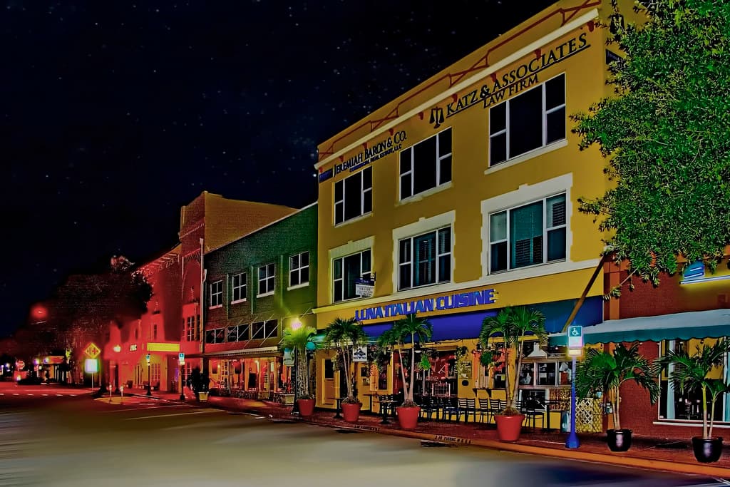Downtown Stuart at night with lit restaurants, colorful storefronts, palm trees, and a walkable Florida main street.