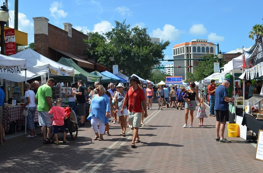 Sarasota Farmers Market with vendor tents, shoppers, and local food stalls along a sunny downtown street.
