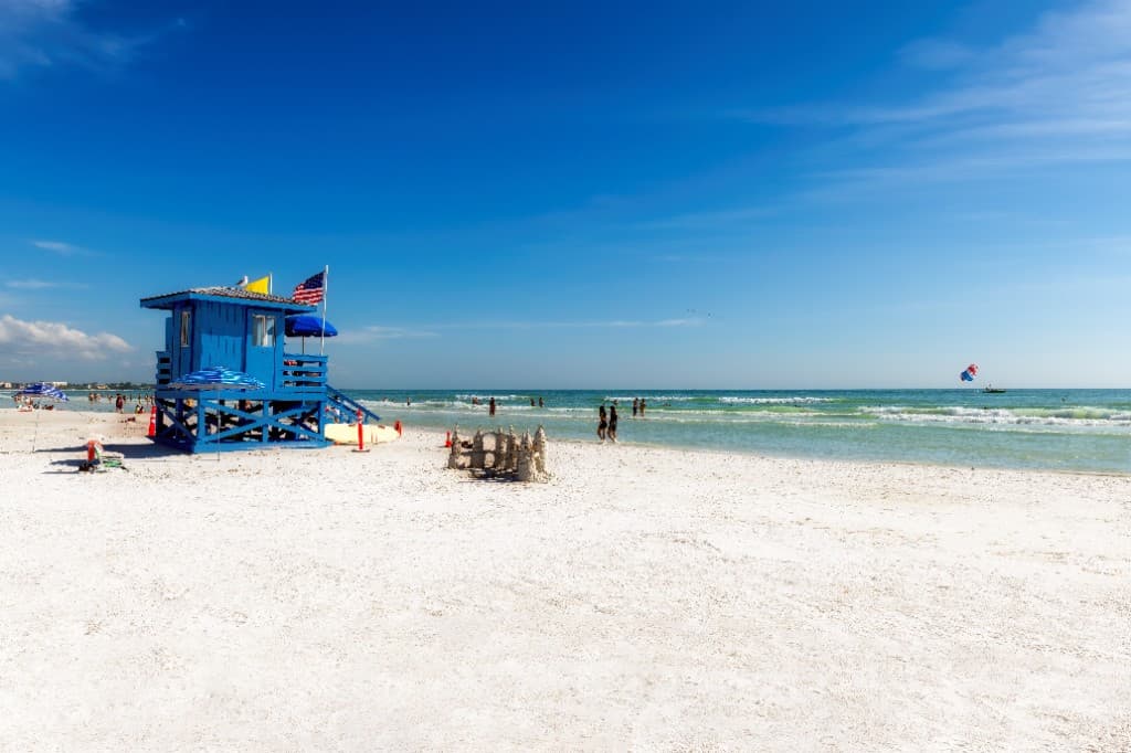 Blue lifeguard stand on Siesta Key Beach with white sand, ocean waves, and beachgoers on a sunny Florida day.